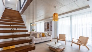 Un soggiorno moderno con una scala, un divano bianco, due poltrone in legno e un tavolino da caffè bianco.