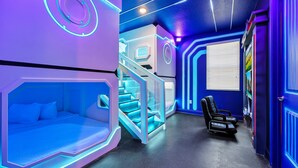 Futuristinen huone, jossa on sänky, hierontatuoli ja portaikko.
