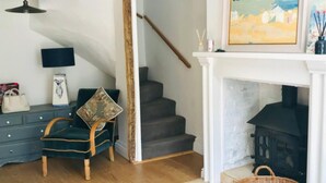 Un salon avec un fauteuil vert foncé, un plancher en bois, un escalier, une cheminée et un tableau accroché au mur.