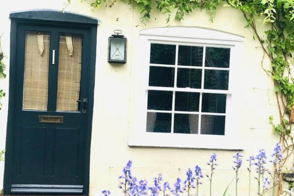 Une maison traditionnelle avec une porte vert foncé, une fenêtre blanche et une lanterne fixée au mur.