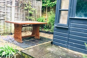 Un banc en bois dans un jardin, avec un bâtiment bleu en arrière-plan.