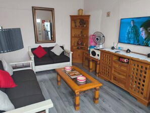 Uma sala de estar com sofá, mesa de centro, televisão, aparador com objetos decorativos e espelho.