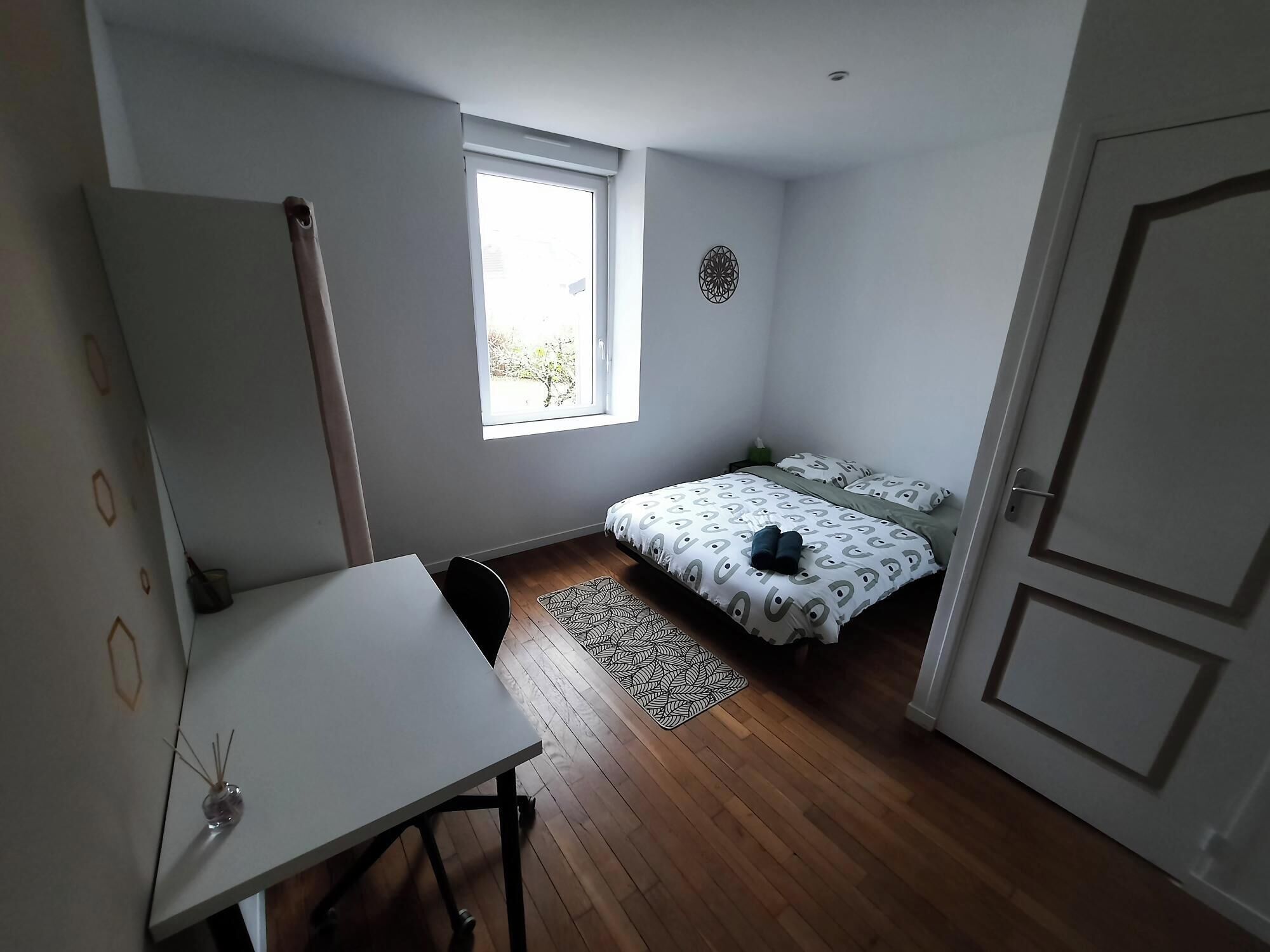 A small, well-lit room with a bed, a desk, and a window.