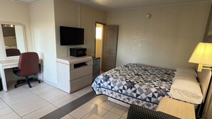 A hotel room with a bed, a desk with a chair, a television, a microwave, and a small refrigerator. - American Inn (Cocoa)