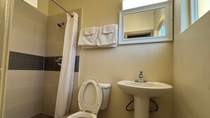 A bathroom with a shower, toilet, sink, and a mirror. - American Inn (Cocoa)