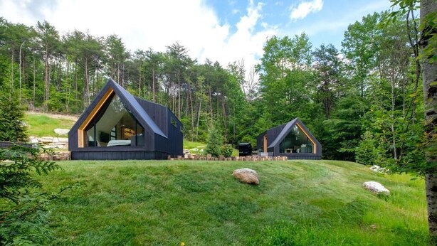 Dos cabañas modernas en un entorno boscoso con una ladera cubierta de césped.