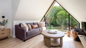Un dormitorio estilo loft moderno con techo inclinado, un ventanal grande con vistas a zonas verdes, una mesa redonda de madera y un sofá morado.