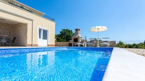 Una piscina con un muro de piedra y una zona de barbacoa.