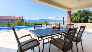 Un espacio al aire libre cubierto con piscina, sillas y una mesa con fruta y copas de vino.