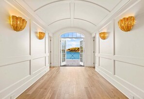A hallway with white walls, wooden flooring, and a view through an open door to a blue railing. - Lakeside Luxury w/Private Heated Pool, Sleeps 15 (Hot Springs)