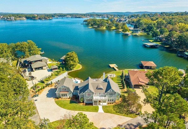 A large house with a driveway, a lawn, and a lake in the background. - Lakeside Luxury w/Private Heated Pool, Sleeps 15 (Hot Springs)