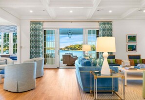 A modern living room with a sofa, chairs, a coffee table, and a view of the sea through large windows. - Lakeside Luxury w/Private Heated Pool, Sleeps 15 (Hot Springs)