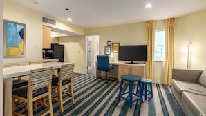 Una habitación de hotel compacta con zona de comedor, kitchenette, televisor y sofá.