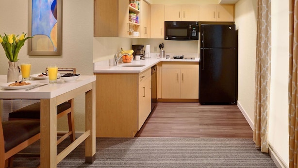 Una cocina compacta con armarios de madera, un refrigerador negro, un microondas y un comedor con una mesa lista para el desayuno.