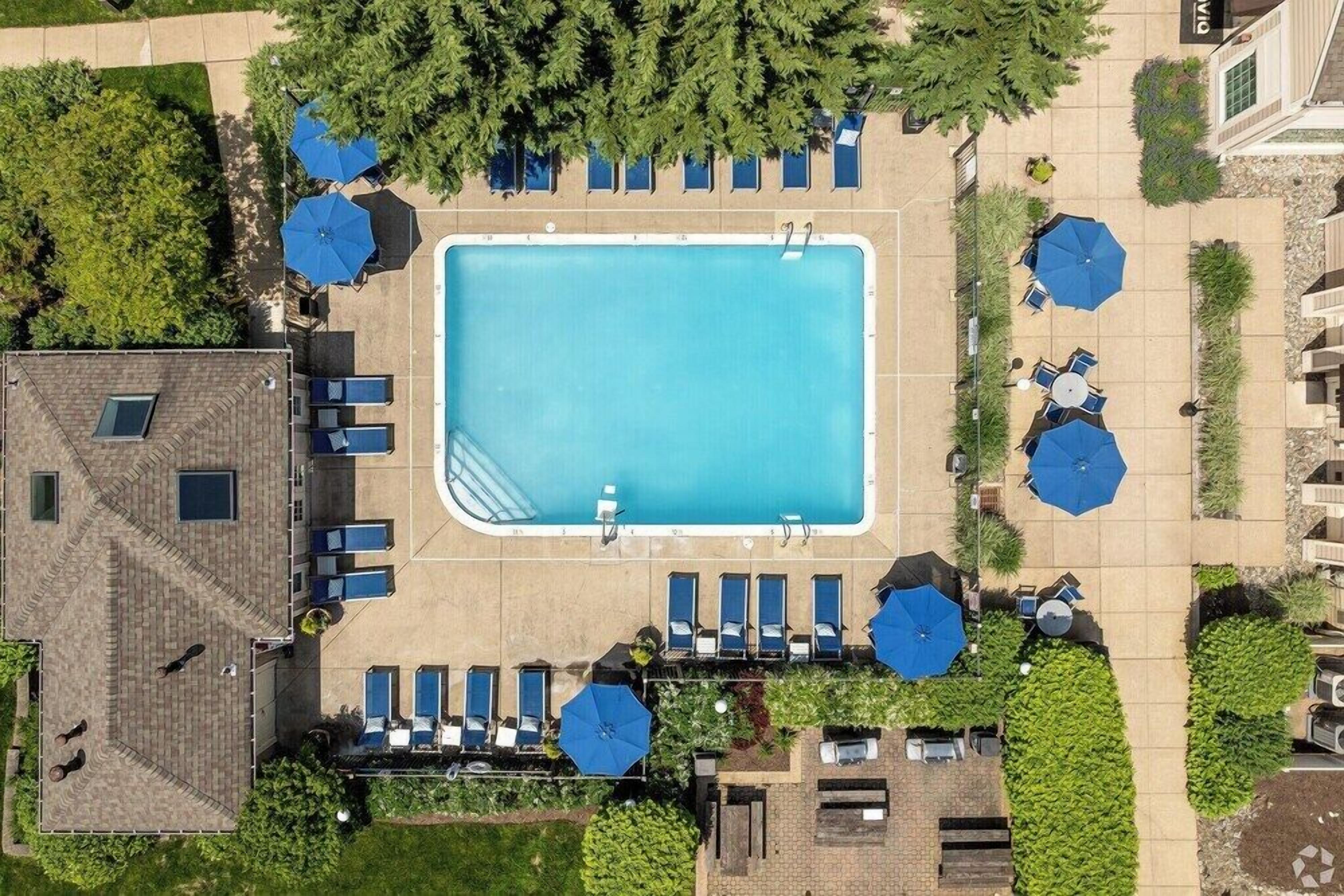 Luftaufnahme eines Hotels mit zentralem Schwimmbecken, Liegestühlen und Sonnenschirmen.