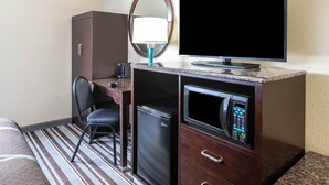 Habitación de hotel con cama, escritorio con computadora, televisor, microondas y refrigerador.