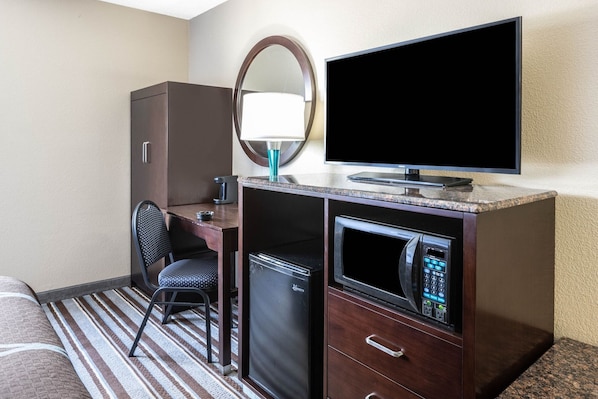 Habitación de hotel con cama, escritorio con computadora, televisor, microondas y refrigerador.