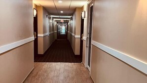 Un pasillo largo y estrecho con suelo de madera y paredes color beige, que conduce a una puerta al final.