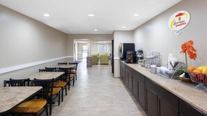 Un comedor de hotel con mesas y sillas largas, una barra de cocina con productos para el desayuno, y un letrero que dice 'Superstart breakfast'.