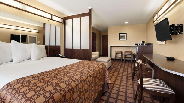 Une chambre d’hôtel avec un grand lit, un bureau avec une chaise, un téléviseur fixé au mur et un petit coin cuisine.