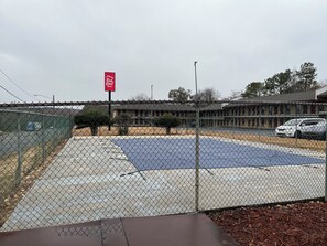 Ein eingezäunter Parkplatz mit einem Red Roof Inn Schild, ein Gebäude mit flachem Dach und ein weißer Wagen in der Nähe.
