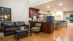 A modern living room with a brown leather sofa, a patterned armchair, a coffee table, and a kitchen area with a breakfast bar. - Red Roof Inn Rockingham (Rockingham)
