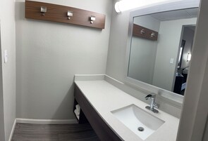 A modern bathroom with a white sink, a large mirror, and a wooden shelf above the sink.