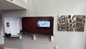 A living room with a flat-screen TV mounted on a dark wall, wooden flooring, and a white door. - Red Roof Inn Rockingham (Rockingham)