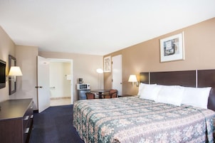 A hotel room with a large bed, a desk with a lamp, a television, and a door leading to a bathroom.