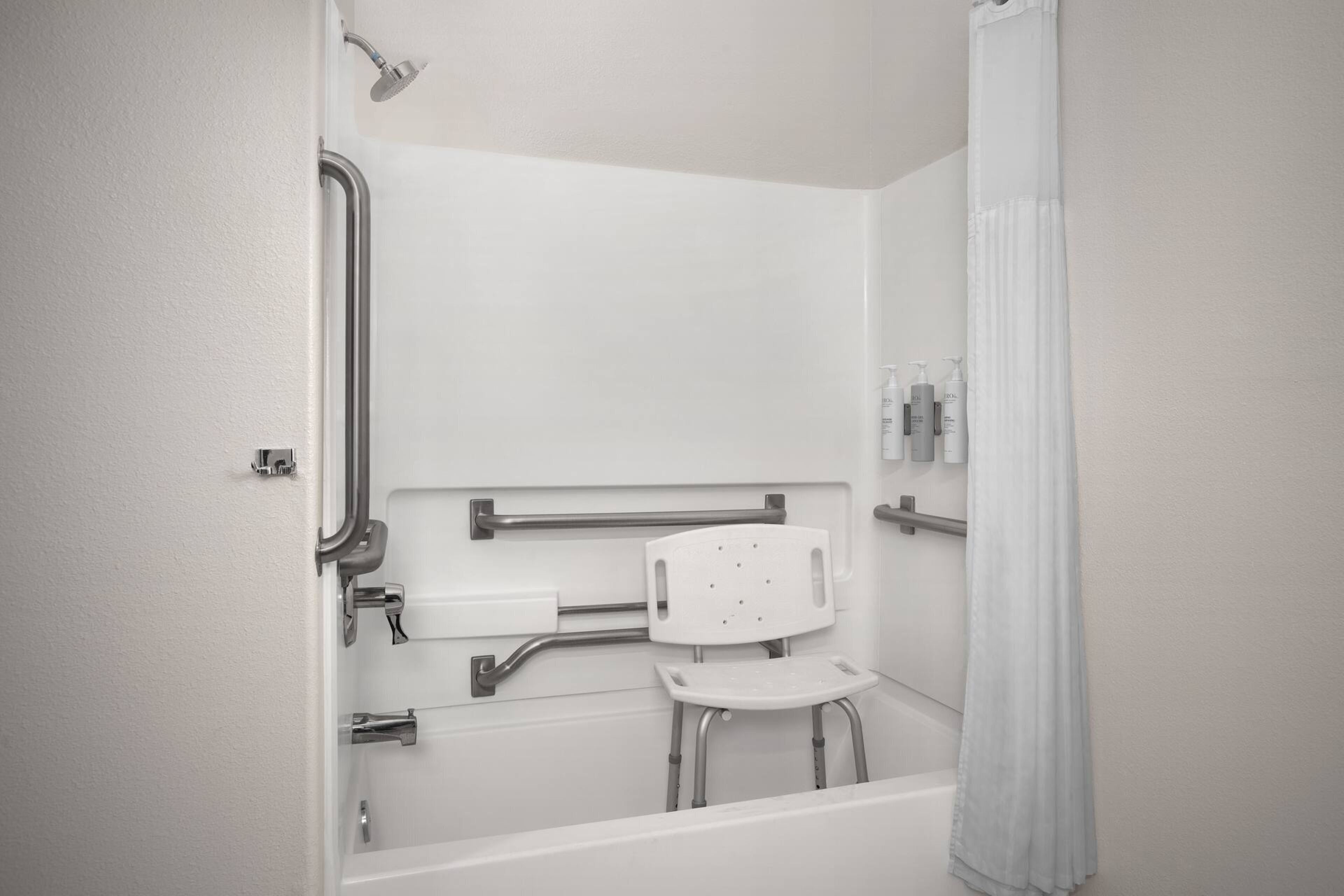 A bathroom with a shower, grab bars, a wheelchair-accessible bench, and a toilet.