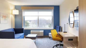 Habitación de hotel con cama, escritorio, silla, ventana con vistas y televisor montado en la pared.