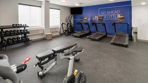 Ein Fitnessstudio mit Laufbändern, Kurzhanteln und einer Bank.