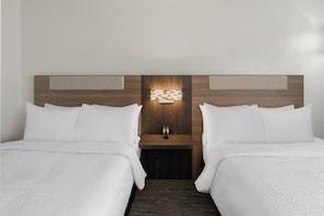 A hotel room with two beds, a nightstand, and a wall-mounted light fixture.