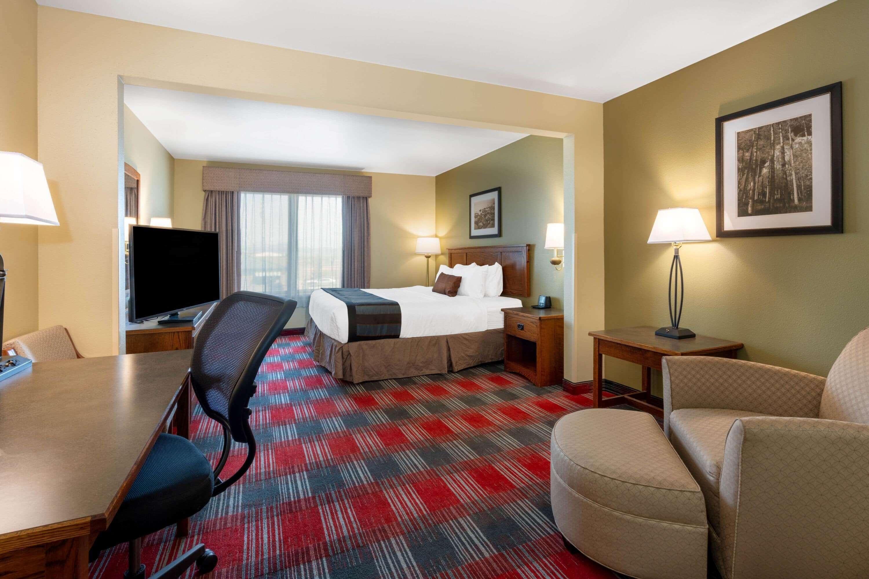 A hotel room with a bed, a desk, a television, two lamps, and a framed picture on the wall.