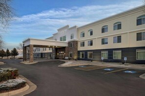 Un hotel con vestíbulo cubierto, varias ventanas y espacios de estacionamiento.