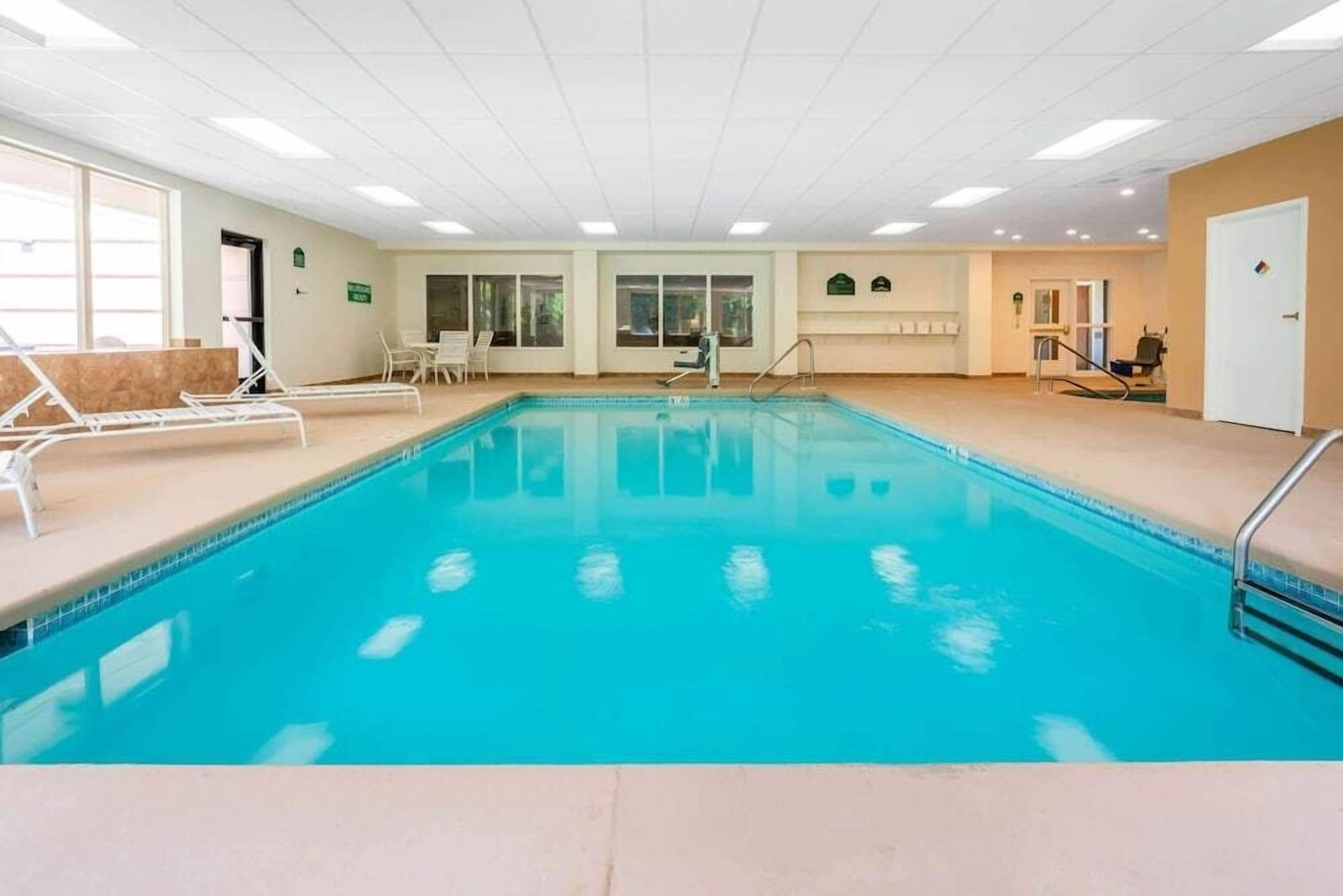 An indoor swimming pool with clear water, surrounded by lounge chairs and a small staircase leading to a door.