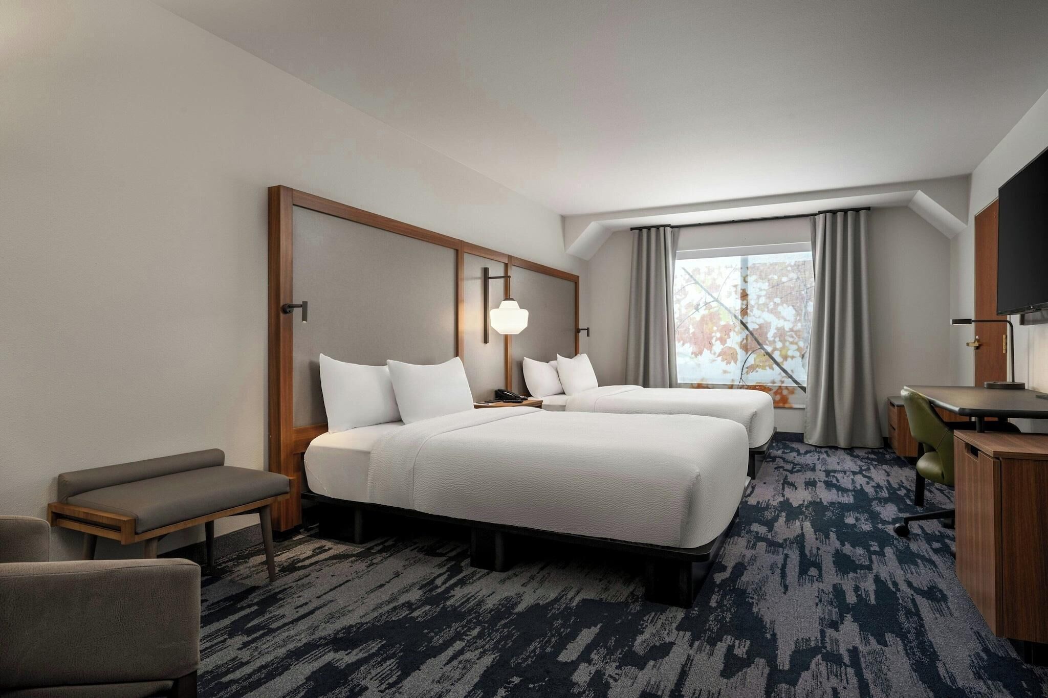 A hotel room with two beds, a desk, a chair, and a television.