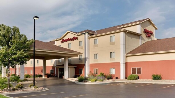 Ett Hampton Inn-hotell med en ingång som är skyddad från väder och vind, en parkeringsplats och en klar himmel.