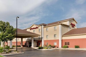 A Hampton Inn hotel with a covered entrance, a parking lot, and a clear sky.