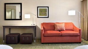A hotel room with a sofa, a desk, a mirror, a lamp, and a framed picture on the wall. - Summit Suites (Gillette)