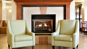 A fireplace with two armchairs in front, a wooden mantel, and a tiled floor. - Summit Suites (Gillette)