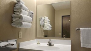 A hotel bathroom with a white sink, a mirror, and towels neatly stacked on the wall. - Super 8 by Wyndham Blackwell (Blackwell)