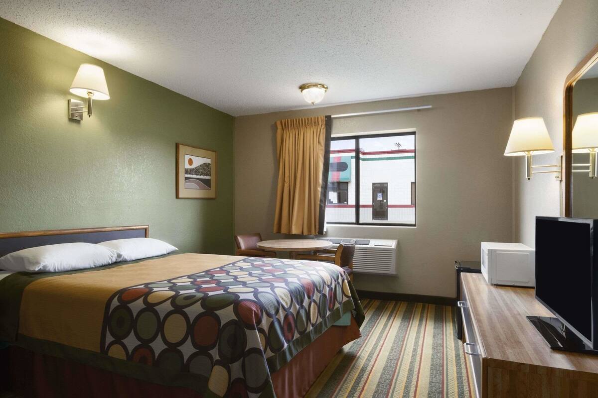 A hotel room with a bed, a desk, a television, a window with curtains, and a picture on the wall.