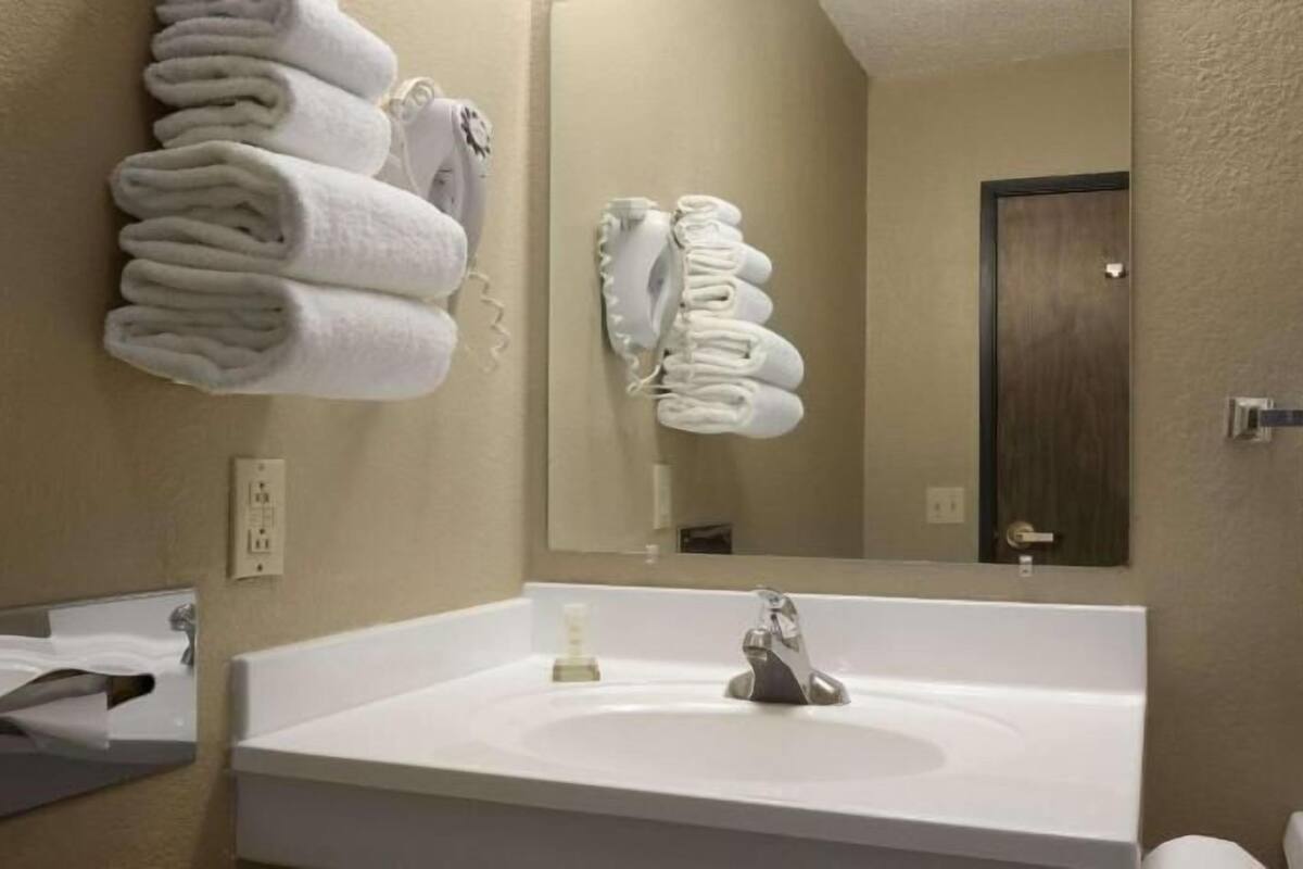 A bathroom with a white sink, a mirror, and towels hanging on the wall.