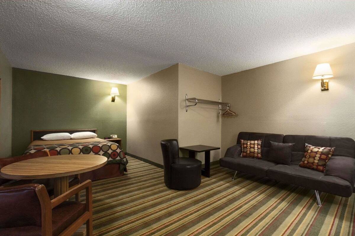 A hotel room with a bed, a sofa, a small table, a chair, and a lamp.