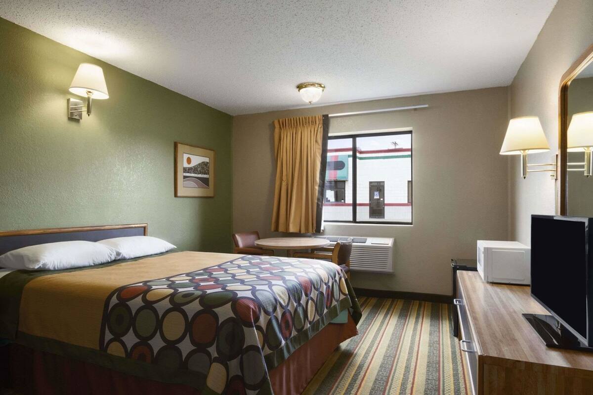 A hotel room with a bed, a desk, a chair, a television, a window with curtains, and a picture on the wall.