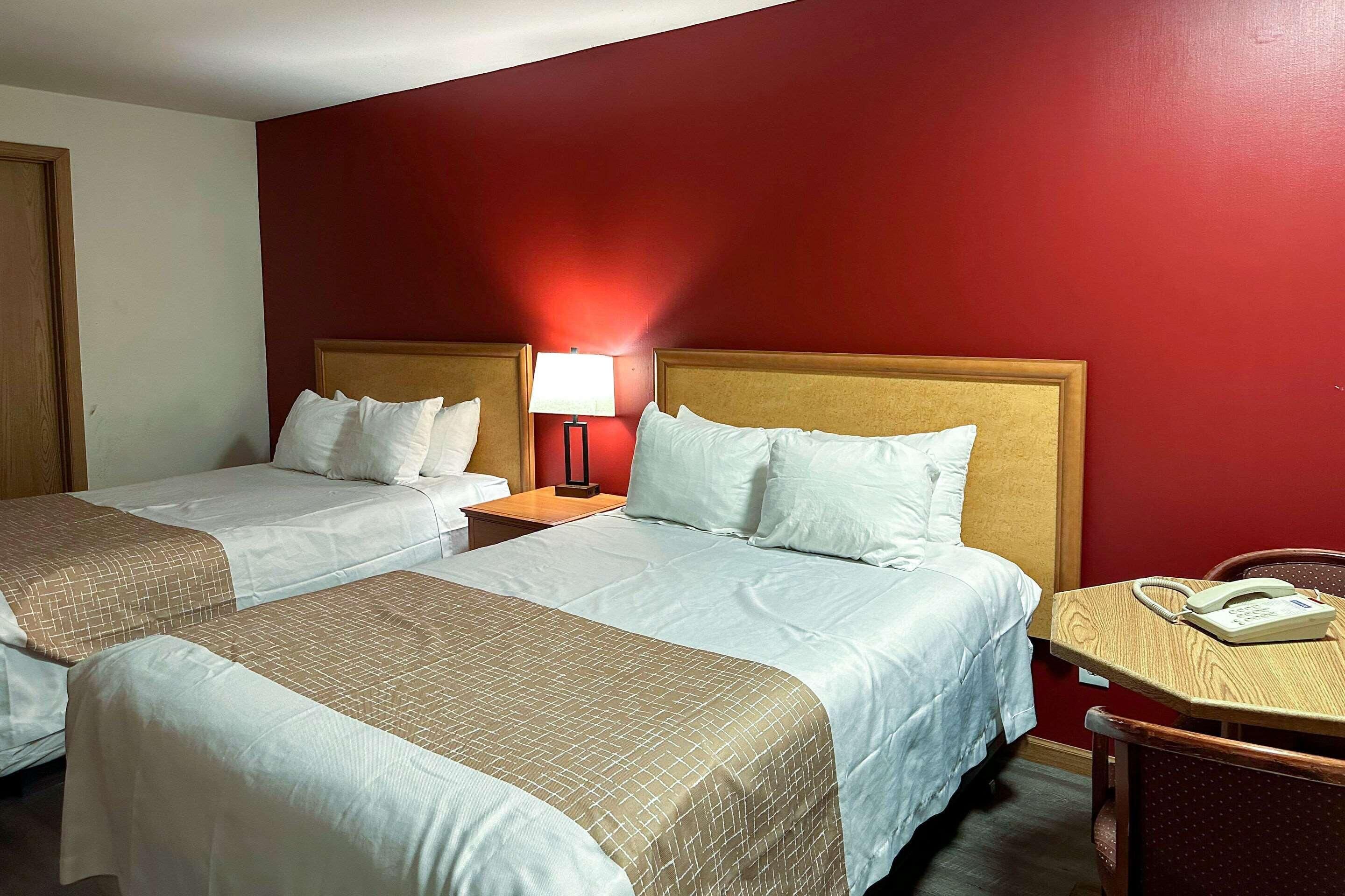 Habitación de hotel con dos camas, cabecero de madera, mesita de noche con lámpara y un teléfono sobre una pequeña mesa.