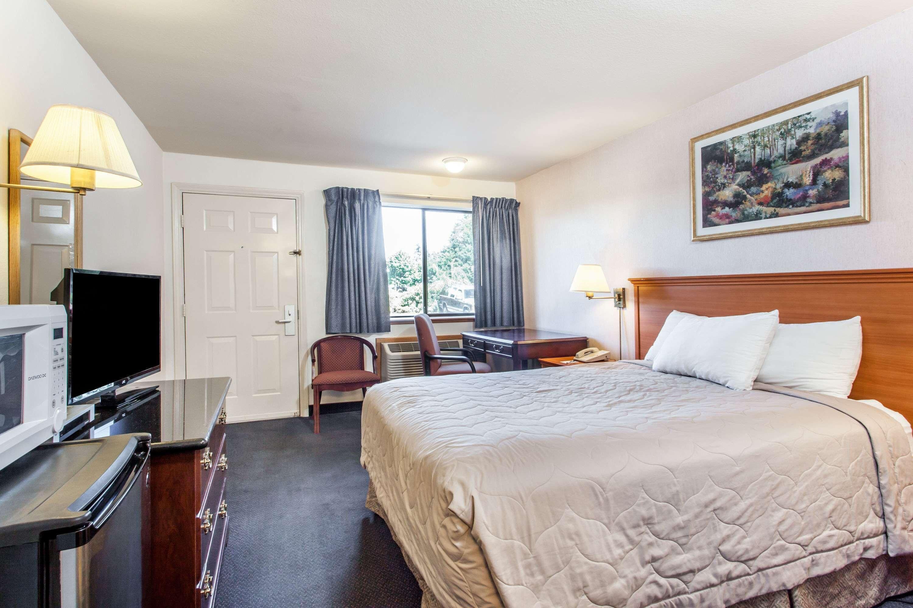A hotel room with a bed, desk, chair, television, and a painting on the wall.