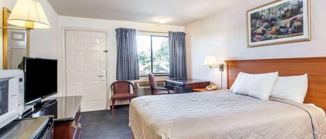 A hotel room with a bed, desk, chair, television, and a painting on the wall.
