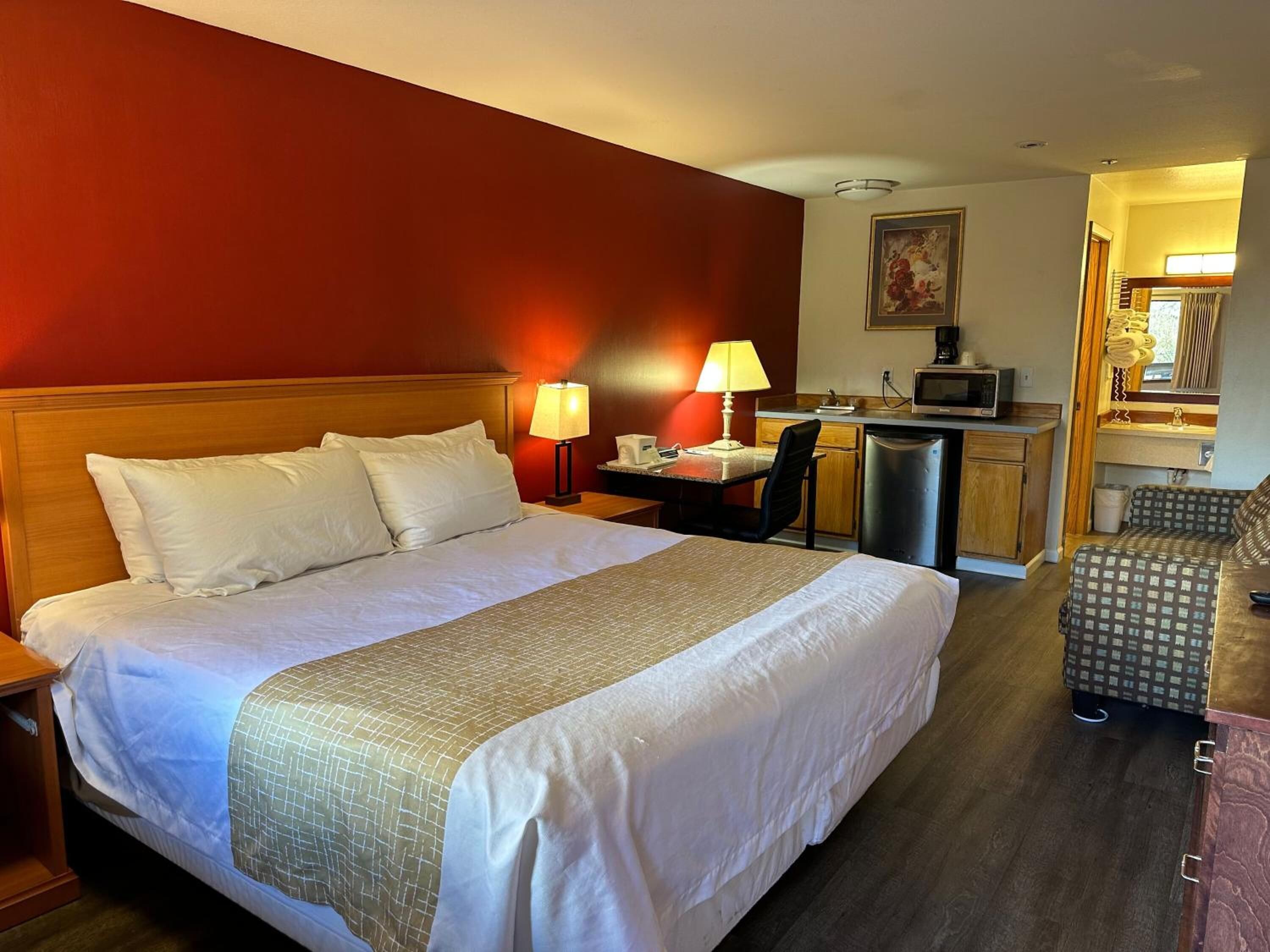 Habitación de hotel con una cama grande, un escritorio con silla, microondas y una pequeña kitchenette.